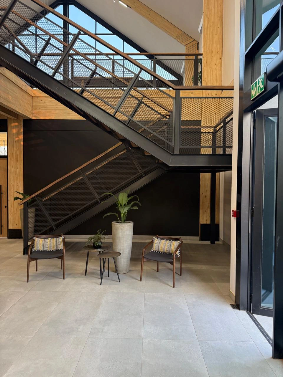 Lounge chairs and a side table beneath the open steel staircase in the double-volume atrium at the Seventh Star venue, with a tall planter alongside