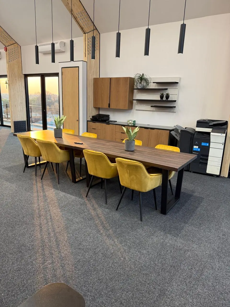 Upstairs boardroom at the Seventh Star venue with a timber table, mustard velvet chairs and pendant lighting, with glass doors at the far end
