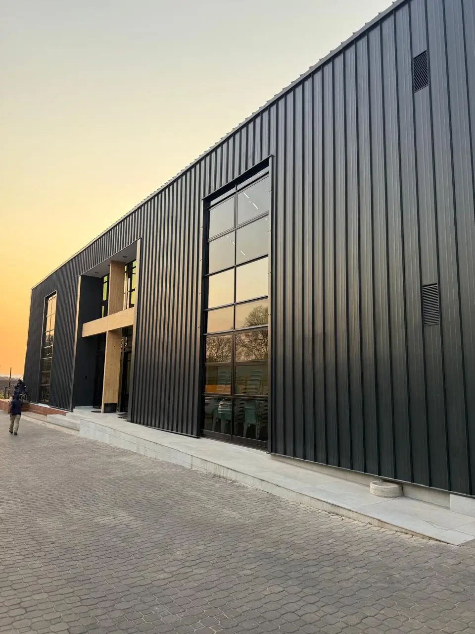 Entrance to the Seventh Star venue at sunset, with a timber-framed doorway set into dark vertical cladding and steps up from the paved forecourt
