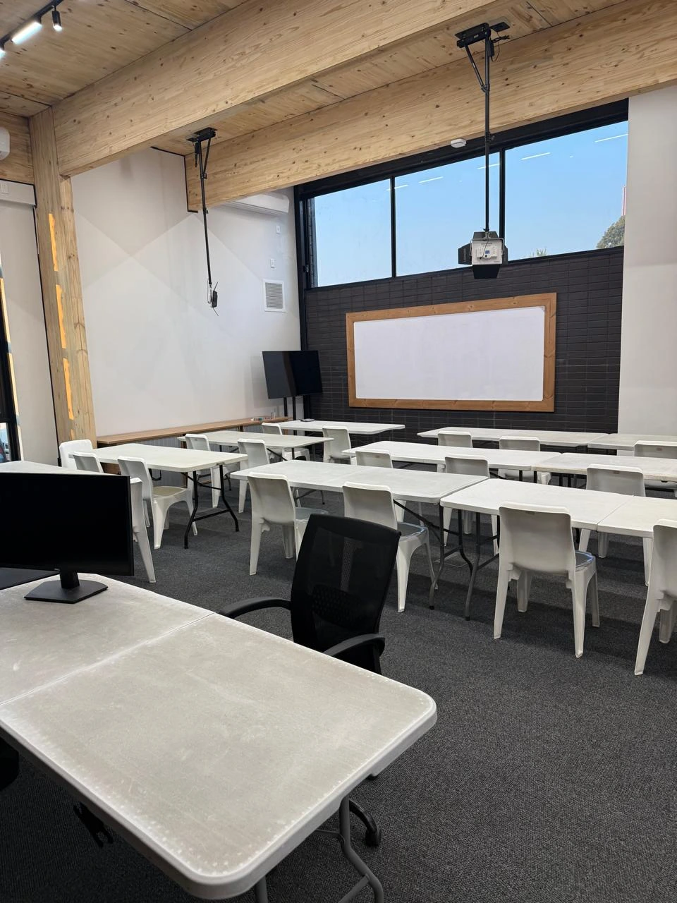 Training room at the Seventh Star venue laid out classroom-style, with rows of tables and chairs facing a large projector screen on a dark feature wall