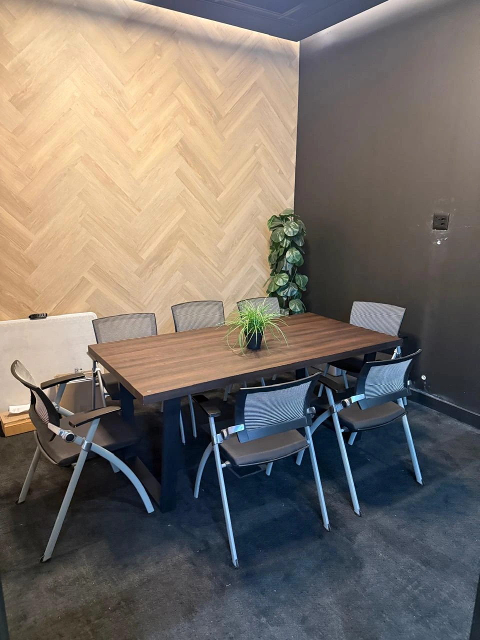 Eight-seater meeting room at the Seventh Star venue with a timber table, mesh-backed chairs, a herringbone timber feature wall and a whiteboard