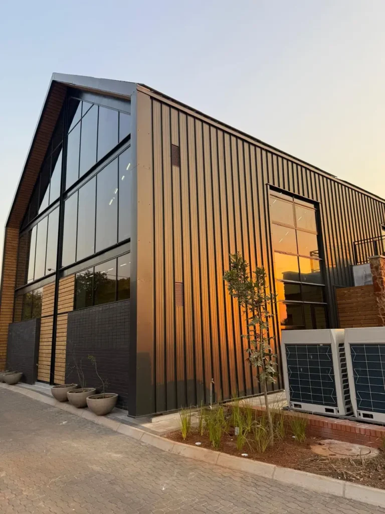 Corner view of the Seventh Star venue at sunset, showing the pitched gable roof, full-height glazing and dark vertical cladding against a paved forecourt
