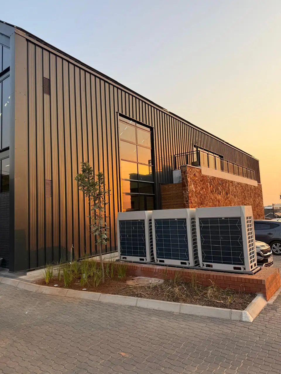 Side elevation of the Seventh Star venue at sunset, clad in dark vertical metal with young landscaping along the paved driveway