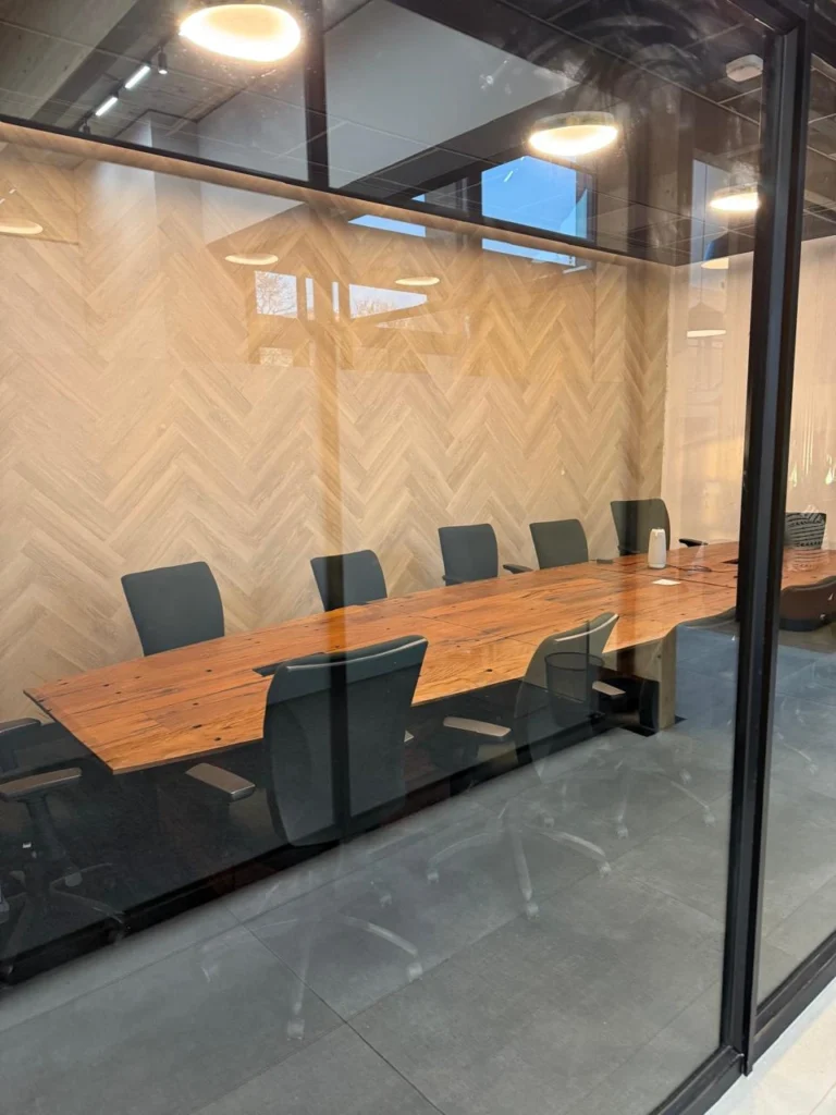 Glass-walled boardroom at the Seventh Star venue with a long reclaimed-timber table, black mesh chairs, a herringbone timber feature wall and circular pendant lights