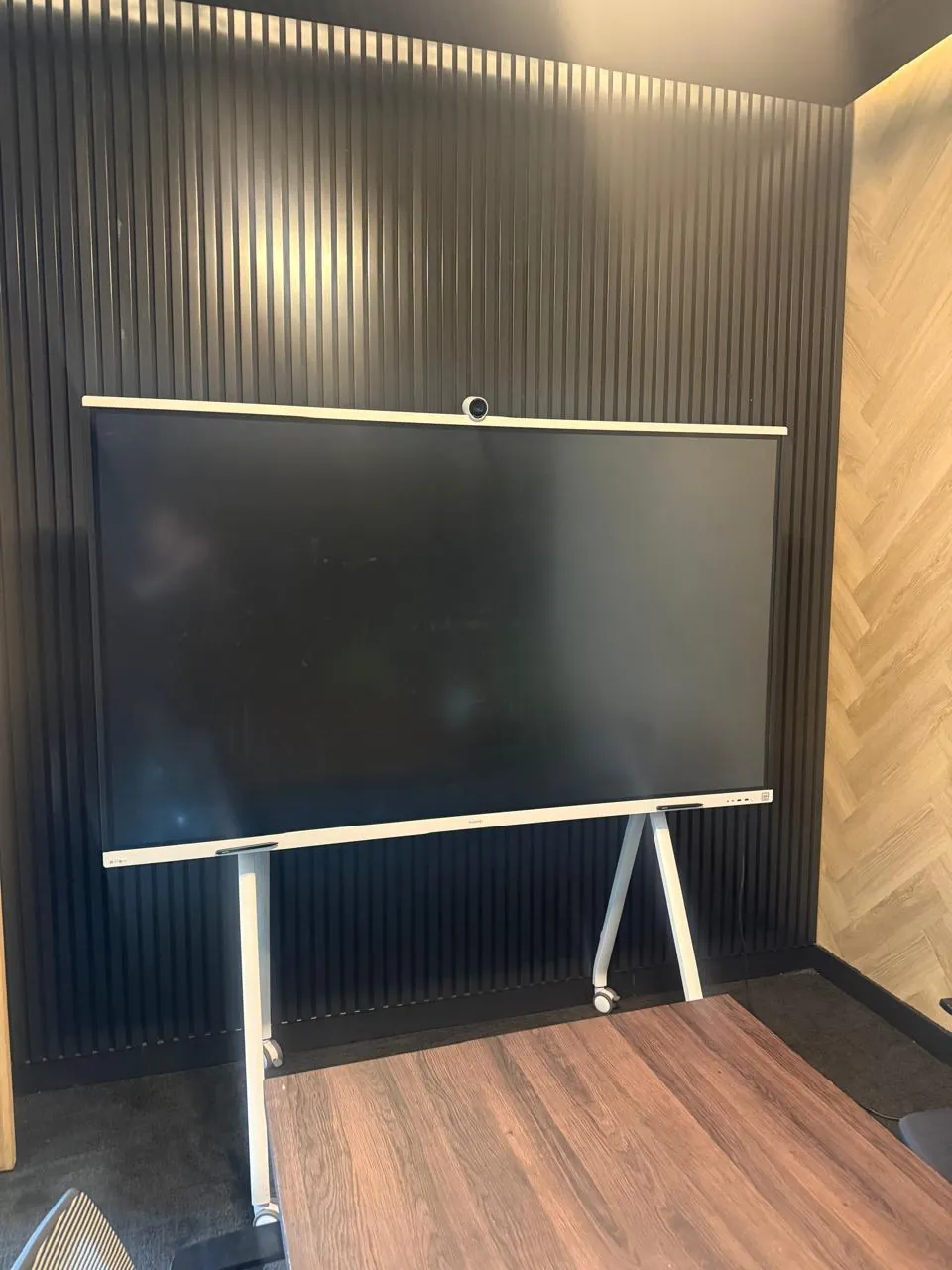 Large flat-screen display with a camera bar on a white mobile stand, set against a black slatted wall at the Seventh Star venue