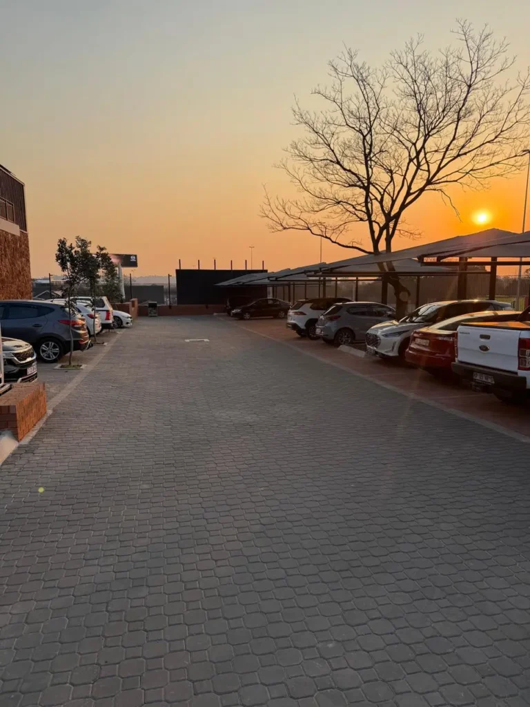 Paved on-site parking at the Seventh Star venue at sunset, with shaded carport bays along one side and open bays alongside the building