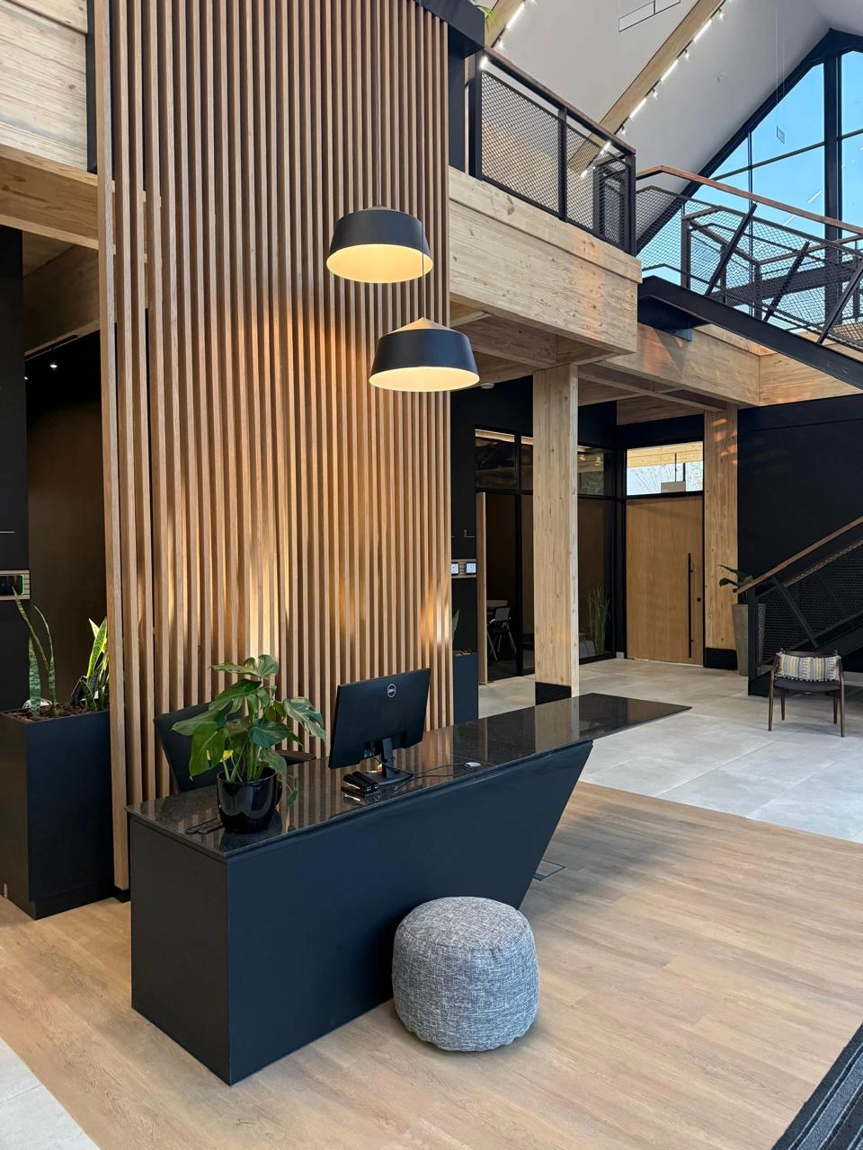 Reception desk at the Seventh Star venue, a black angular counter set against a timber slat wall beneath two black pendant lights, with the mezzanine above