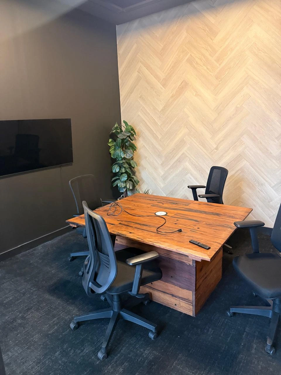 Small meeting room at the Seventh Star venue with a reclaimed timber table, four mesh office chairs, a wall-mounted screen and a herringbone timber feature wall