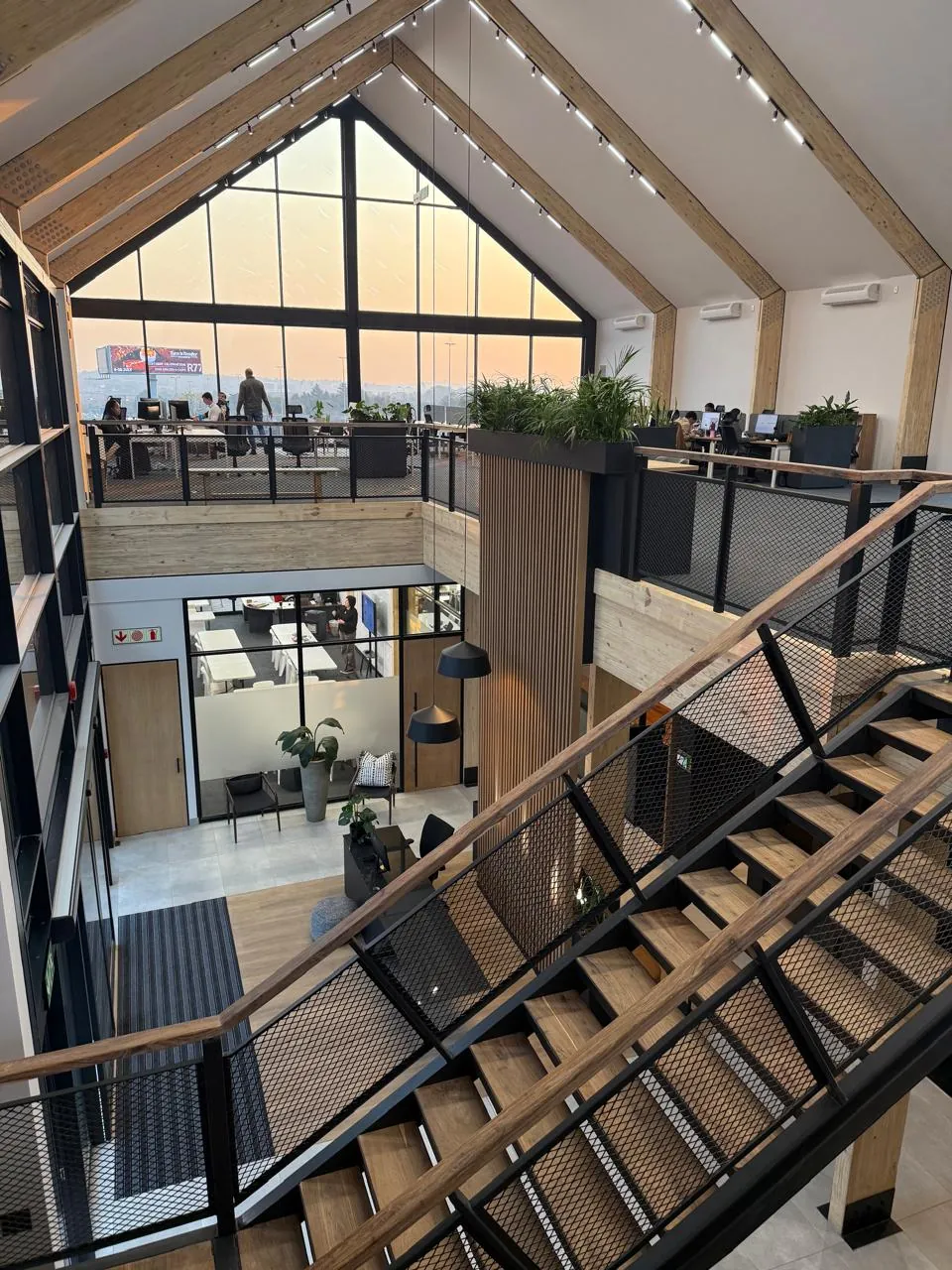 Timber and black steel staircase at the Seventh Star venue, viewed from the mezzanine looking down to the reception area, with a gable window and workspace behind