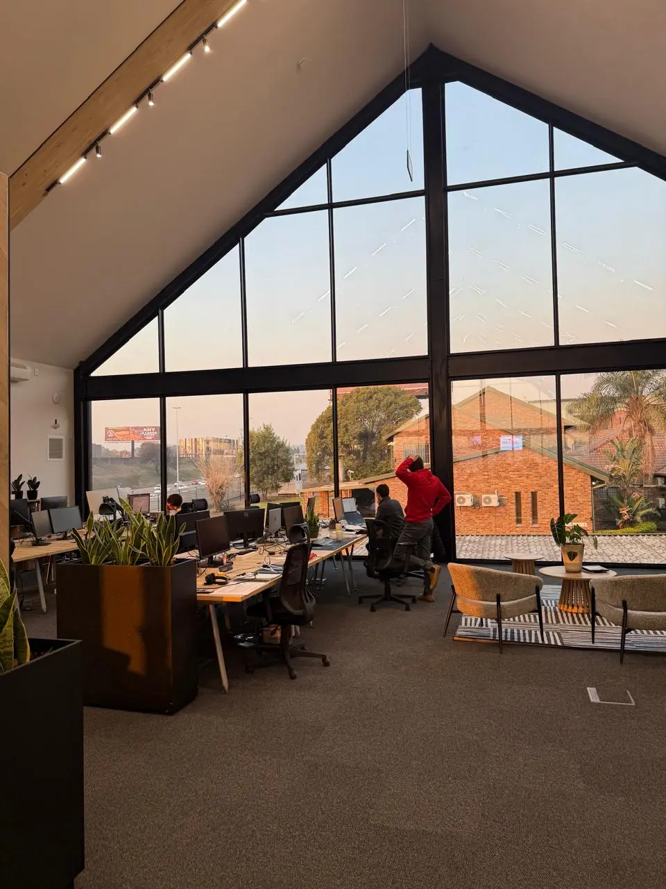 Upstairs open-plan workspace at the Seventh Star venue under a vaulted timber ceiling, with desks facing a full-height gable window overlooking rooftops and trees